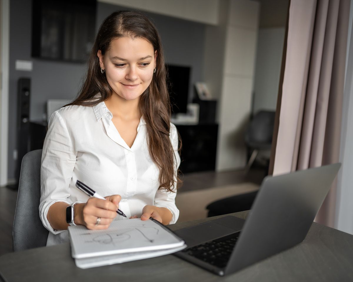 A professional taking notes beside a laptop